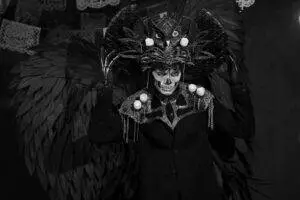 Person dressed in elaborate Day of the Dead costume with skull makeup and feathered wings.