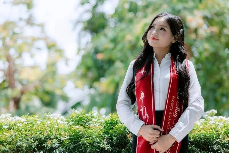 Proud young graduate wearing red stole in garden setting on a bright day.