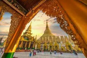 Vibrant scene at Shwedagon Pagoda with people walking around ornate golden structures at sunset.